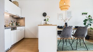 A modern kitchen with white cabinets, a wooden countertop, and a dining area with two chairs and a table.