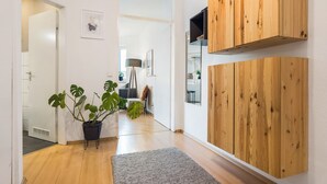 A hallway with a potted plant, a grey rug, wooden wall panels, and a door leading to another room.