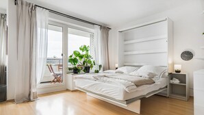 A modern bedroom with a bed, a bedside table, a nightstand, a window with curtains, and a view of the outside.