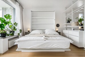Ein modernes Schlafzimmer mit einem großen Bett, Nachttischen, einer integrierten Regaleinheit und Topfpflanzen.