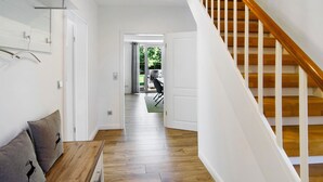 Ein Flur mit Holzboden, weißen Wänden, einer Holztreppe und einer Tür, die zu einem Außenbereich führt.