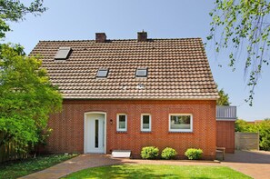 Une maison en briques rouges, avec un toit en tuiles, une porte d’entrée, deux fenêtres et un petit porche.