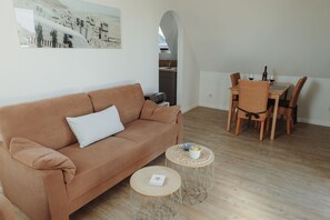 A living room with a sofa, two round tables, a dining table with chairs, and an archway leading to a kitchen.