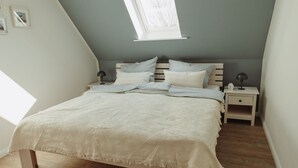 A bedroom with a sloped ceiling, a skylight, a bed with a white bedspread, two bedside tables with lamps, and a wooden floor.