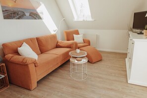 Una sala moderna con un sofá, una pequeña mesa redonda y un televisor sobre un mueble.