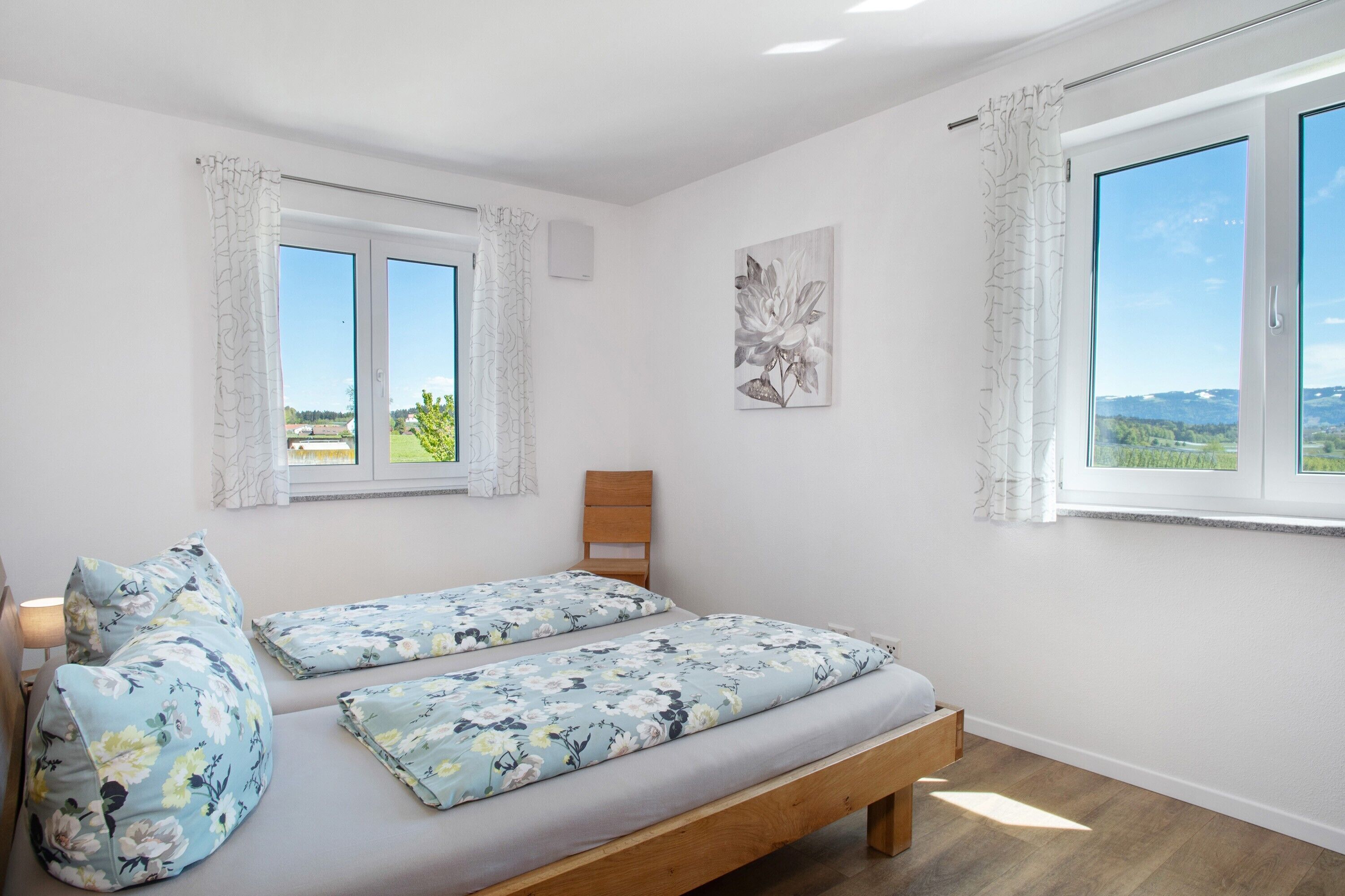 A bedroom with two beds, a wooden headboard, a window with curtains, a wall-mounted light, and a landscape view.
