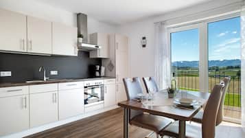 Une cuisine moderne avec des meubles blancs, un coin repas comprenant une table et des chaises, et une grande fenêtre donnant sur un paysage verdoyant.