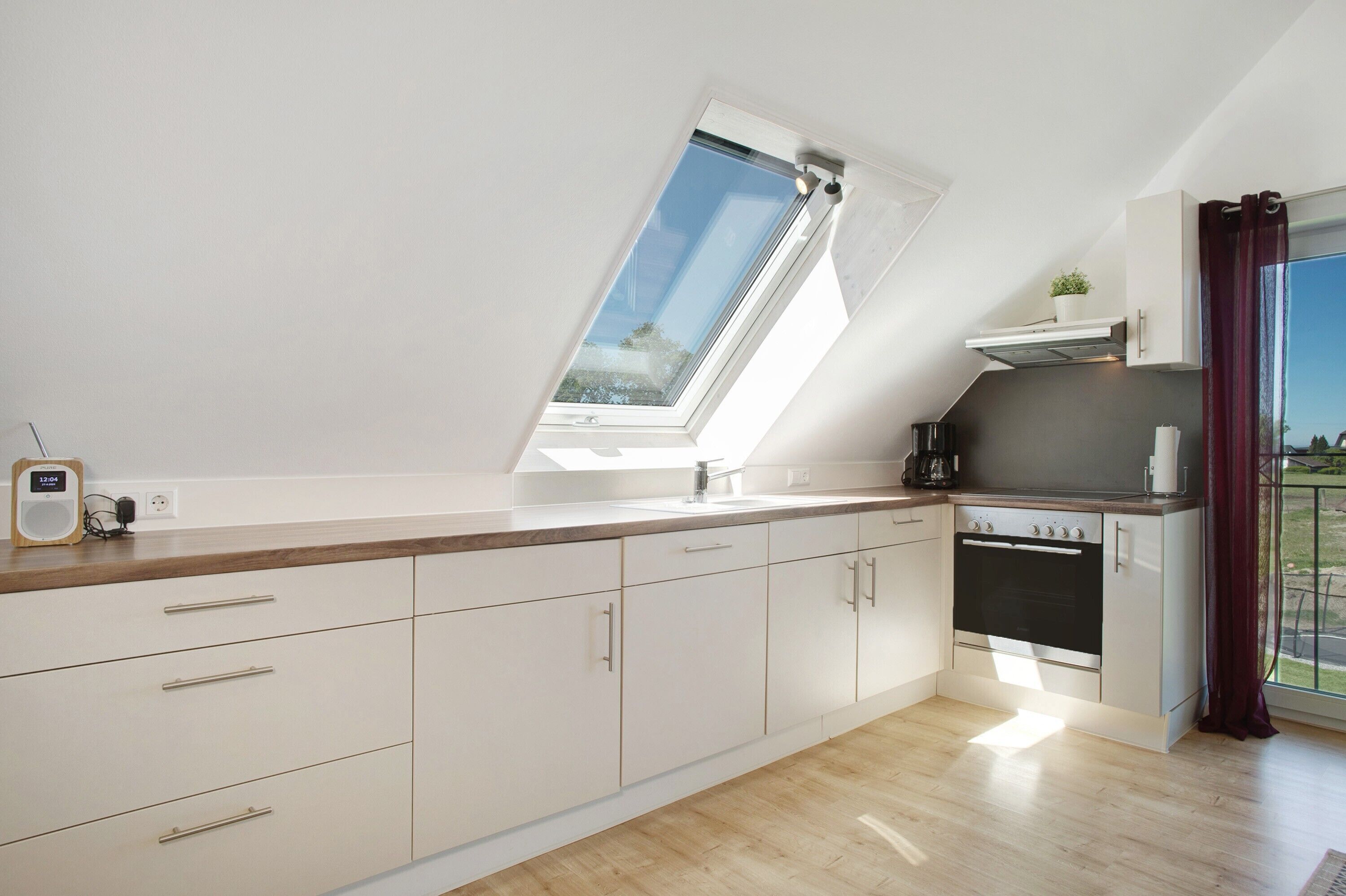 Une cuisine moderne dotée d’une verrière, de meubles blancs, d’un four encastré et offrant une vue sur l’extérieur.
