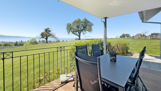 A terrace with a table and chairs, a view of a grassy field, and a tree. - Apartment '2' with Lake View, Shared Garden and Wi-Fi (Kressbronn am Bodensee)