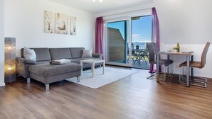 A modern living room with a sofa, a dining table with chairs, a large sliding glass door, and artwork on the wall. - Apartment '2' with Lake View, Shared Garden and Wi-Fi (Kressbronn am Bodensee)