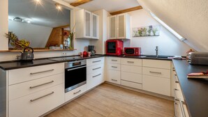 A modern kitchen with white cabinets, a black countertop, and a red microwave. - Holiday Apartment 'Schwarzwald Chalet - Karlshütte' with Mountain View, Private Terrace & Wi-Fi (Gütenbach)