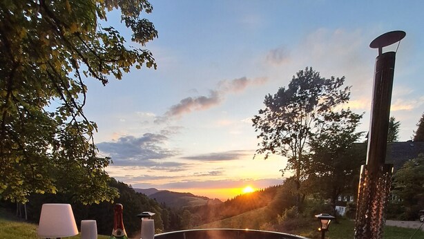 A hot tub with a table and chairs, a bottle, and a glass, set outdoors with a sunset view. - Holiday Apartment 'Schwarzwald Chalet - Karlshütte' with Mountain View, Private Terrace & Wi-Fi (Gütenbach)