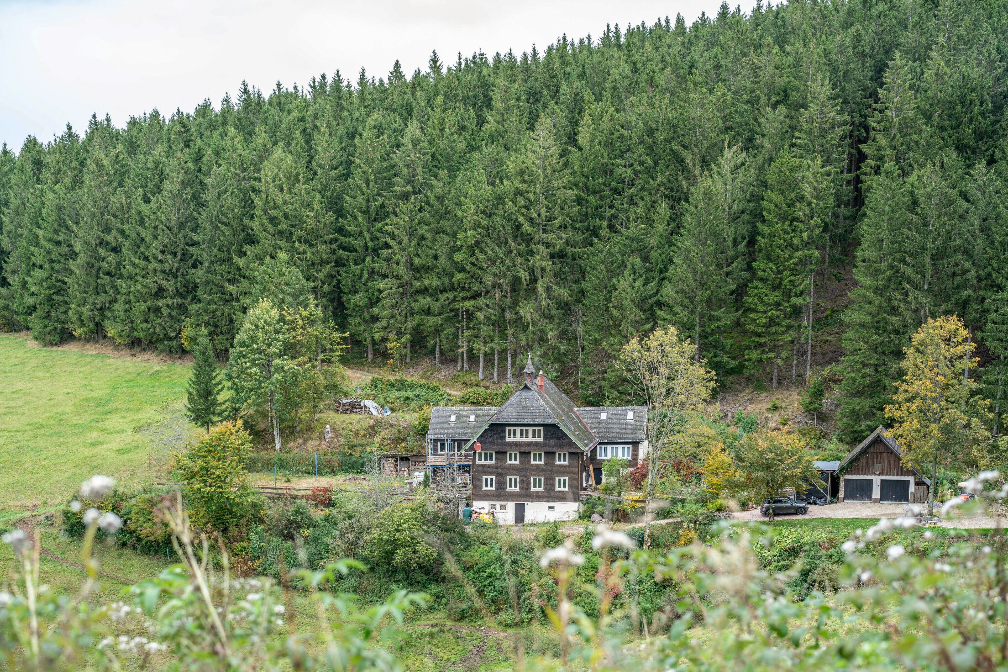 A large house surrounded by dense forest, with a garage and a driveway visible.