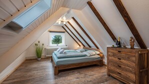 A sloped ceiling room with a bed, wooden dresser, and a radiator. - Holiday Apartment 'Schwarzwald Chalet - Karlshütte' with Mountain View, Private Terrace & Wi-Fi (Gütenbach)
