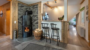 A modern kitchen with a built-in wood stove, a bar area with stools, and a stone wall. - Holiday Apartment 'Schwarzwald Chalet - Karlshütte' with Mountain View, Private Terrace & Wi-Fi (Gütenbach)