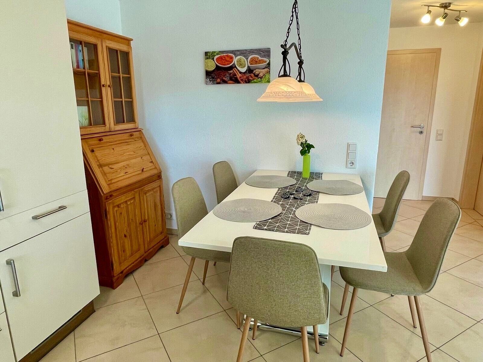 Un espace repas comprenant une table blanche, des chaises grises, un meuble en bois et un luminaire fixé au mur.