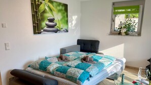 A bedroom with a bed, a glass table, a window with a plant, and a painting on the wall. - Apartment "Am Berg" with Panoramic Views, Terrace, Grill, Parking (Müllheim im Markgräflerland)