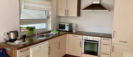 Une cuisine moderne équipée d’un lave-vaisselle, d’un four à micro-ondes, d’une cuisinière et d’une fenêtre avec des stores.