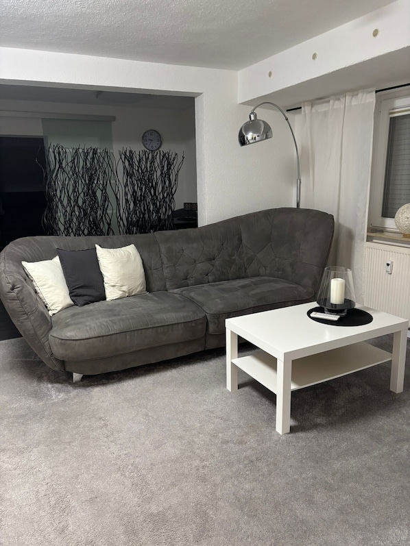 A living room with a grey sofa, a white coffee table, a floor lamp, and a window with curtains.