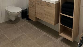 Een badkamer met toilet, wastafel met spiegel, houten kast met lades en een plank met handdoeken.