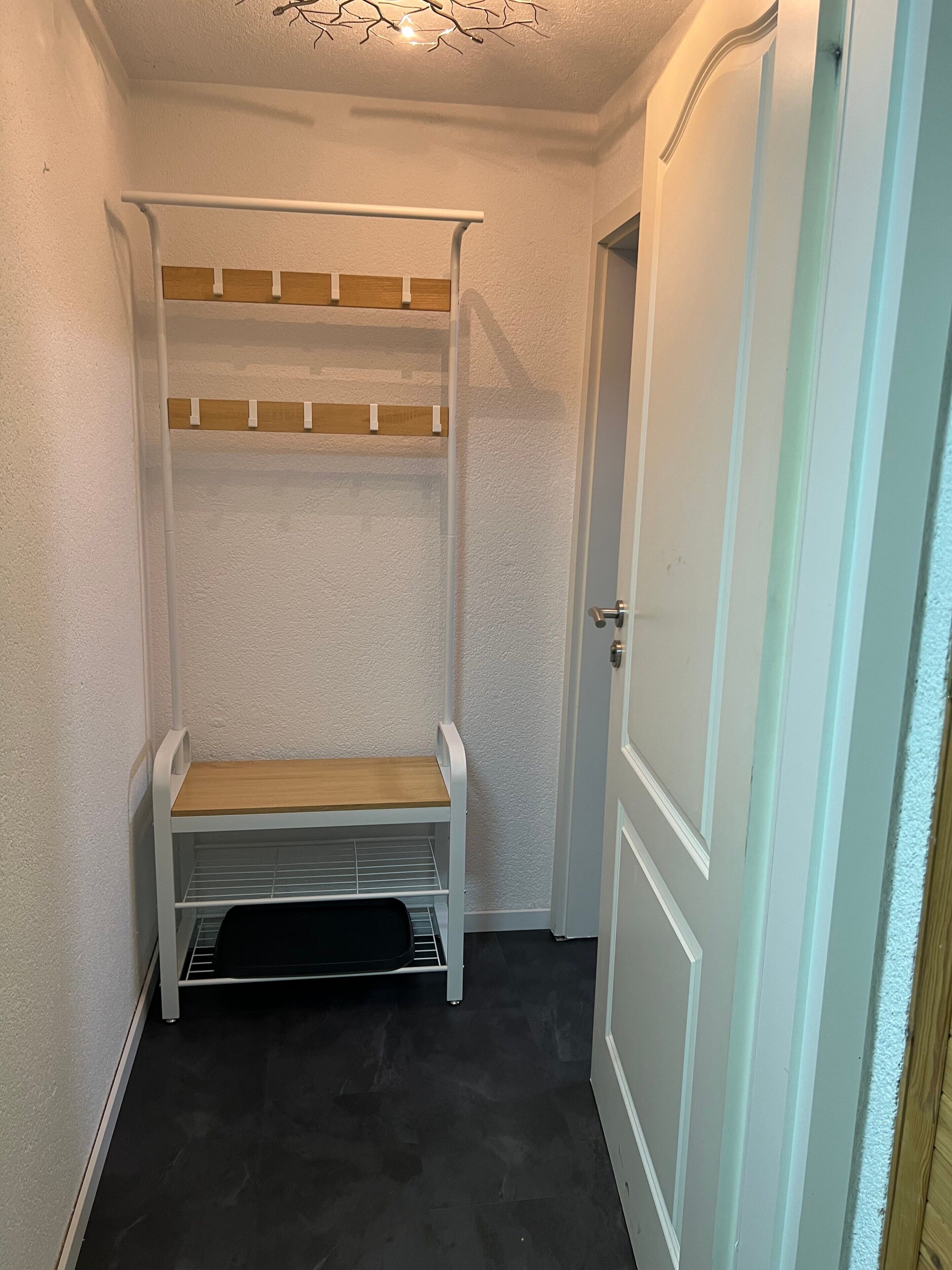 Un pasillo estrecho con un banco blanco con tapa de madera, una puerta blanca y una lámpara en el techo.