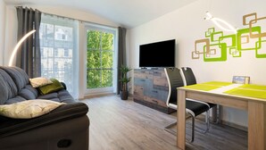 Un salon moderne comprenant un canapé, une table à manger, un téléviseur à écran plat et une grande fenêtre donnant sur un paysage verdoyant.