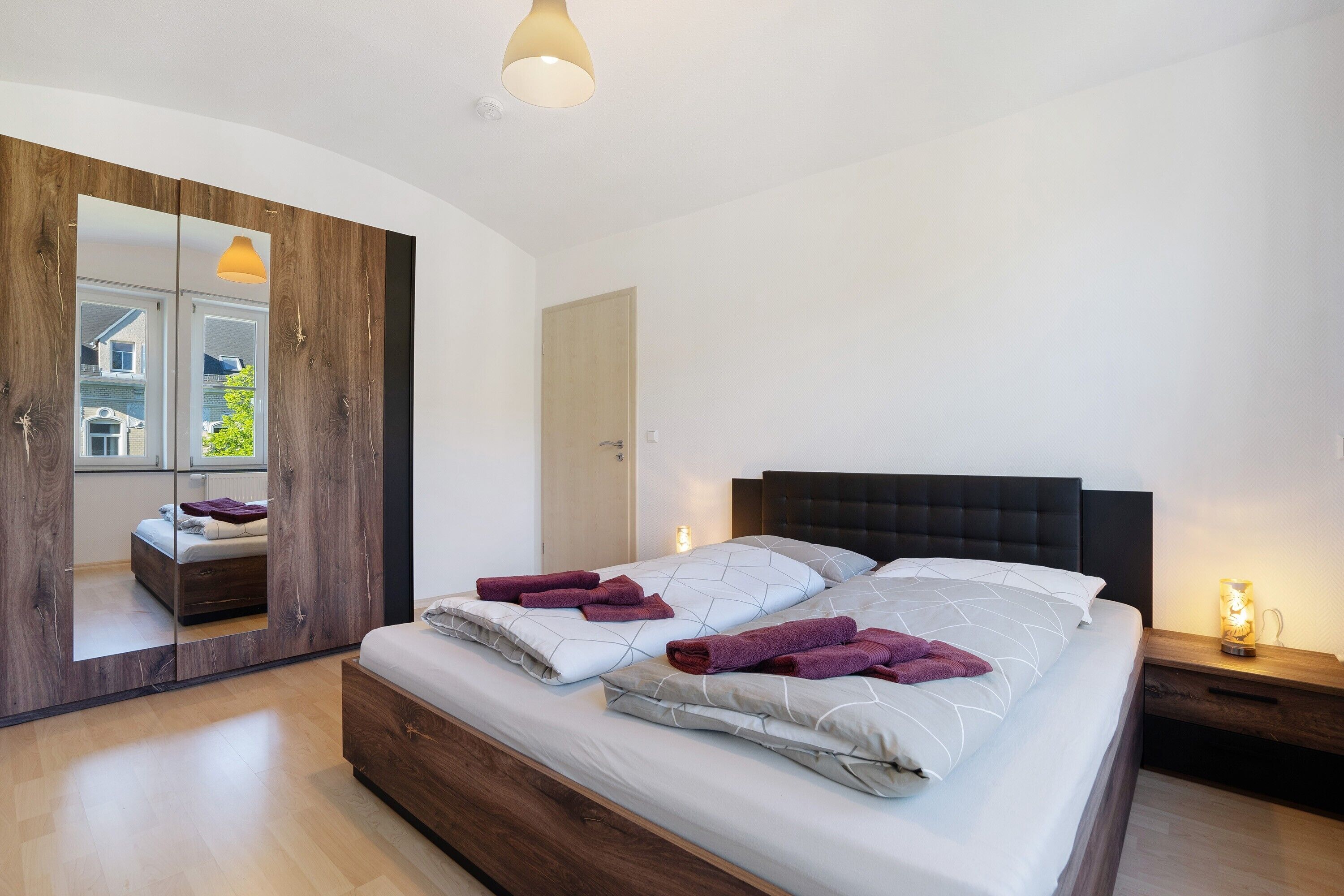 Ein modernes Schlafzimmer mit einem großen Bett, einem Holzschrank und einem Spiegel.