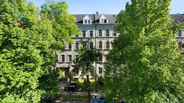 Un immeuble à plusieurs étages, doté d’une entrée centrale et entouré d’arbres verdoyants.