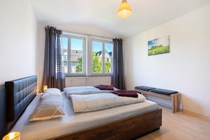 A bedroom with a bed, a bench, a window, and a painting on the wall.