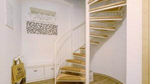 Un escalier blanc avec des marches en bois et une rampe blanche, menant à un palier où se trouve une armoire blanche et une œuvre d’art abstraite accrochée au mur.