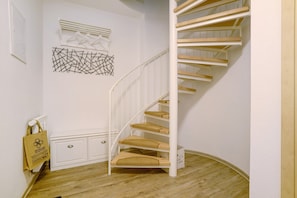 Una escalera blanca con escalones de madera y barandilla blanca, que conduce a una plataforma con un armario blanco y una obra de arte abstracto colgada en la pared.