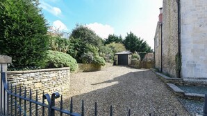 A gravel driveway leading to a building with a stone wall and a metal fence. - Beautiful Georgian Cottage near Frome (Beckington)
