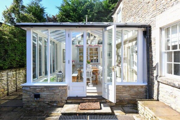 A conservatory with glass doors, a stone wall, and a stone floor. - Beautiful Georgian Cottage near Frome (Beckington)