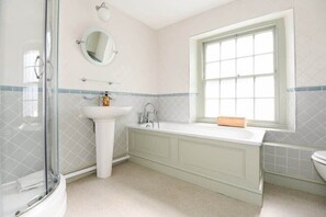 A bathroom with a glass shower enclosure, a pedestal sink, a freestanding bathtub, and a window.
