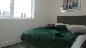 A bedroom with a bed, a window, and a painting on the wall.