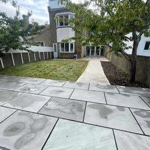 A paved patio with a grassy area and a building in the background. - Margate Garden Apartment (Margate)