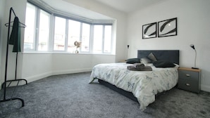 Une chambre à coucher avec un lit, une table de chevet, une lampe, une fenêtre et un porte-manteau.