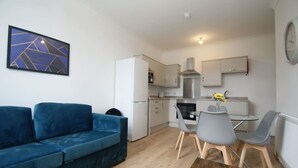 Un espace de vie compact comprenant un canapé bleu, une table à manger avec des chaises, un coin cuisine et une horloge murale.