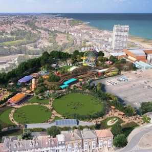 An aerial view of a coastal amusement park with various rides, green spaces, and a large building with a red roof. - Snug Margate Apartment (Margate)