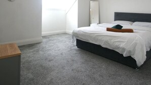 A bedroom with a sloped ceiling, a skylight, a bed with white bedding, a dark headboard, and a small bedside table. - Snug Margate Apartment (Margate)