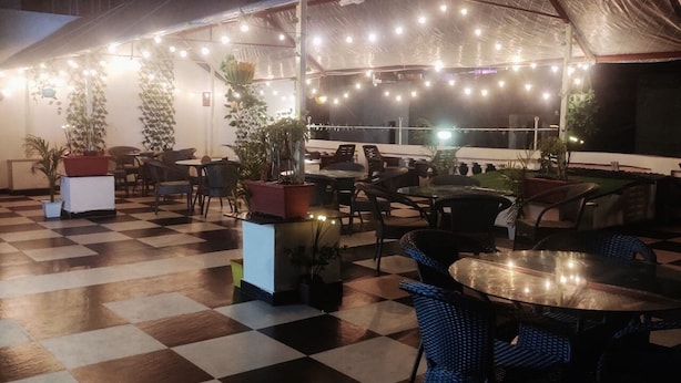 Un patio al aire libre con suelo a cuadros, mesas, sillas, plantas en macetas y luces colgantes.