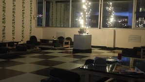 Una habitación con piso de cuadros, un sofá, una mesa con papeles y una ventana adornada con luces colgantes.