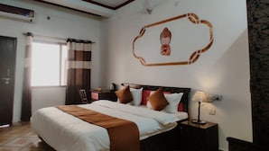 Habitación de hotel con cama, mesita de noche, lámpara, ventana con cortinas y un adorno en la pared.