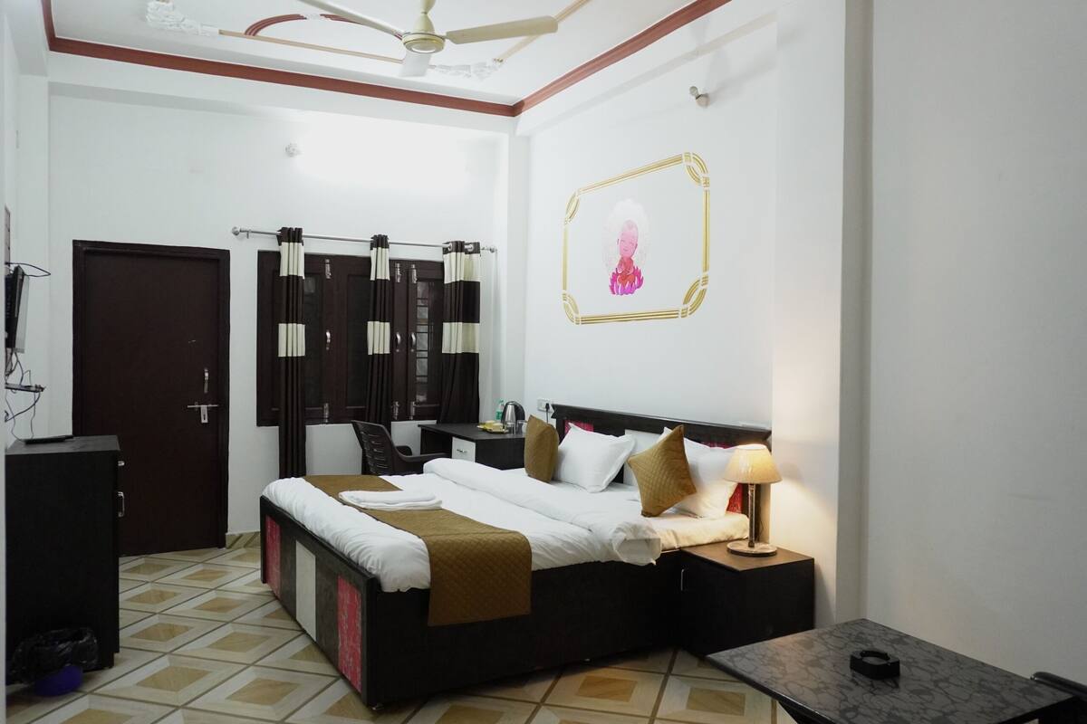 Ein Hotelzimmer mit Bett, Nachttisch, Lampe, Schreibtisch, Stuhl, Kleiderschrank und Deckenventilator.