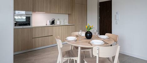 A modern kitchen with wooden cabinets, a built-in oven, and a dining area with a round table and chairs.