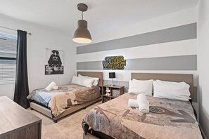 Ett hotellrum med två sängar, en vägg dekorerad med Star Wars-motiv, en hänglampa och ett fönster med gardiner.