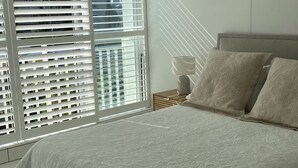 Un dormitorio con una cama grande, una mesita de noche, una lámpara y una ventana con persianas.