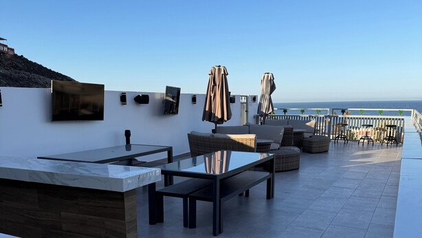 Une terrasse sur le toit, avec une table en verre, des chaises en osier et une balustrade blanche donnant sur la mer.