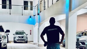 Un agent de sécurité se tient dans un parking, avec des voitures garées de part et d’autre.