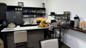 Une cuisine moderne dotée d’un îlot central, d’un four à micro-ondes et de divers appareils de cuisine. On y trouve des chaises et une table avec un plateau en verre.